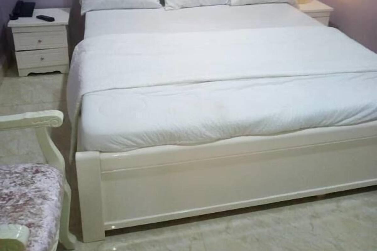 A neatly made bed with white bedding, a headboard with a tufted design, and a bedside table with a lamp.