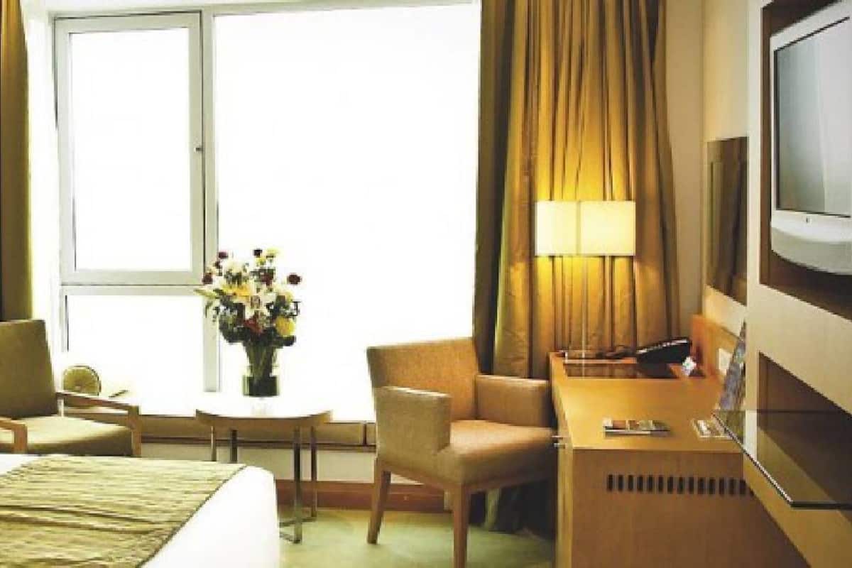 A hotel room with a bed, two chairs, a small table with a vase of flowers, a desk with a computer, and a TV.