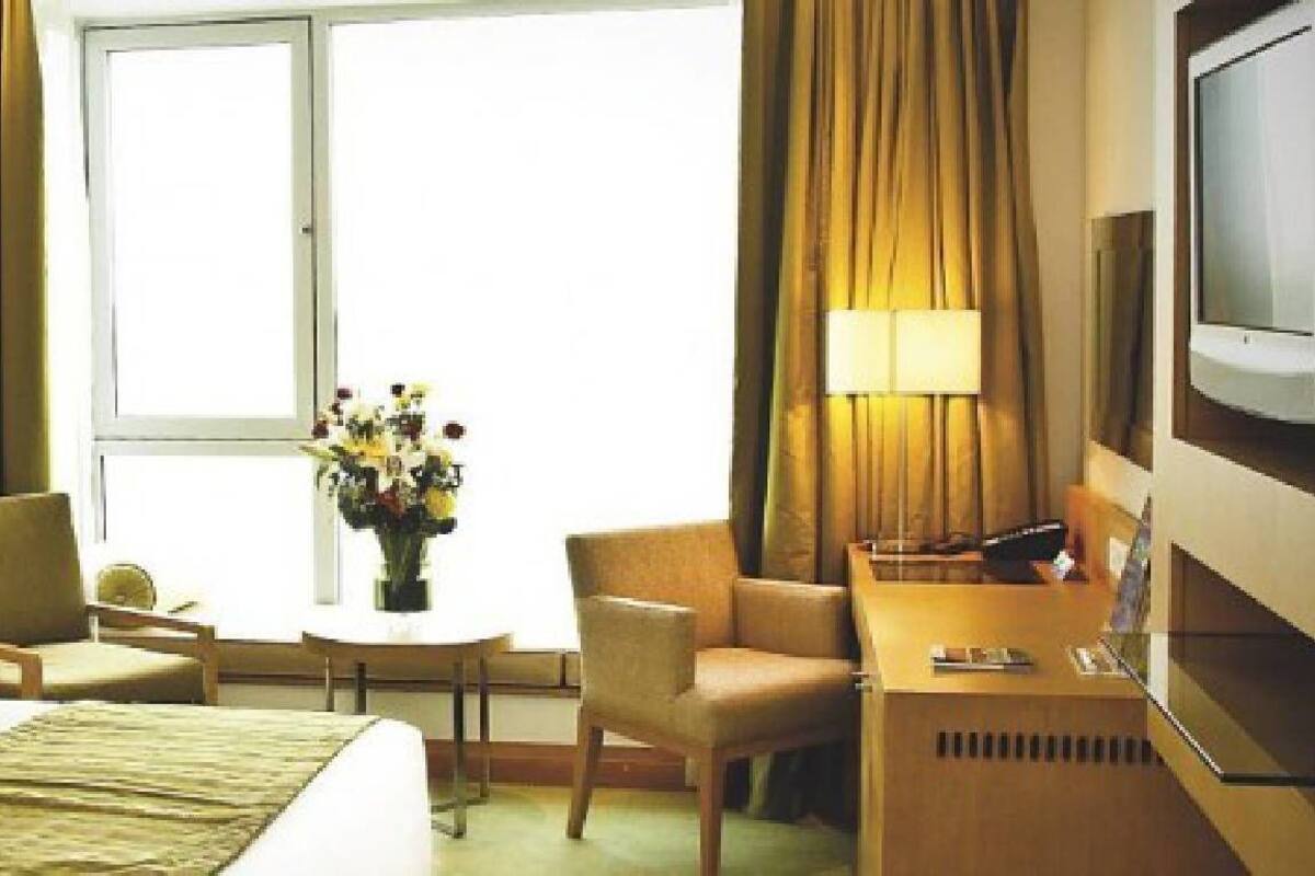 A hotel room with a bed, two chairs, a small table with a vase of flowers, a desk with a computer, and a TV.