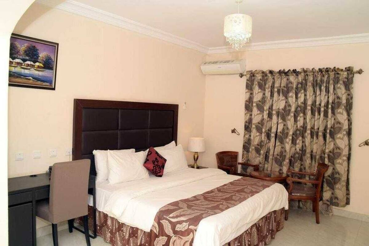 Une chambre d’hôtel avec un lit, un bureau, une chaise, une table et un tableau au mur.