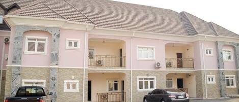 A multi-story residential building with a pink facade, stone accents, and a tiled roof.