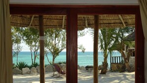 A beach view through a wooden door with a thatched roof, palm trees, and a sandy beach. - Laguna Blu - Resort Madagascar (Andavadoaka)