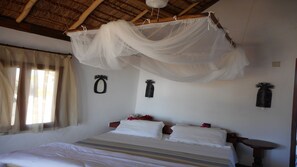 A bedroom with a bed, a mosquito net, and a small bedside table. - Laguna Blu - Resort Madagascar (Andavadoaka)