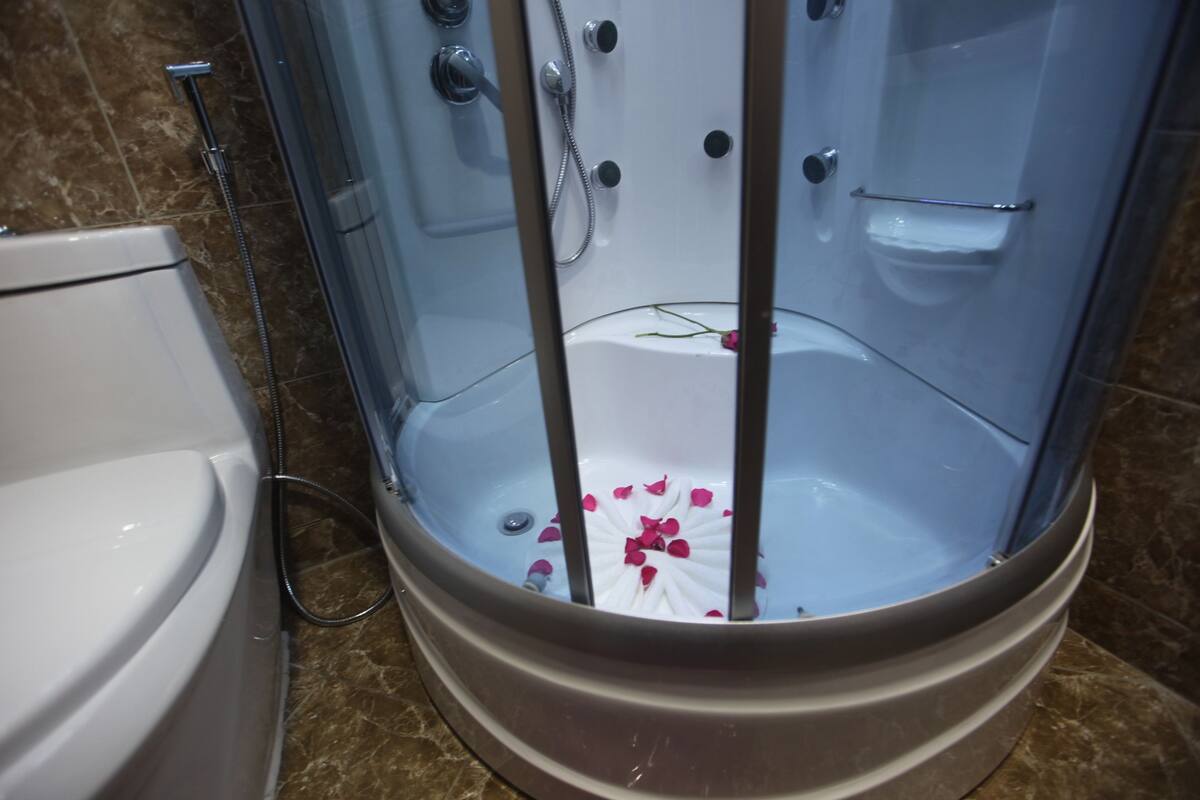 A bathroom with a shower enclosure, a toilet, and a marble floor.