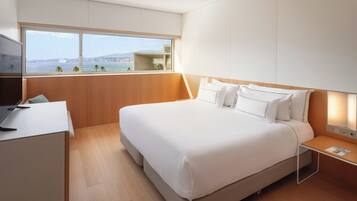 Una habitación de hotel moderna con una cama grande, un escritorio, un televisor y vista al mar.