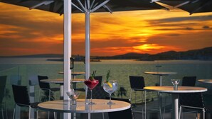 Vista del atardecer desde un restaurante con mesas y sillas, y dos bebidas sobre las mesas.