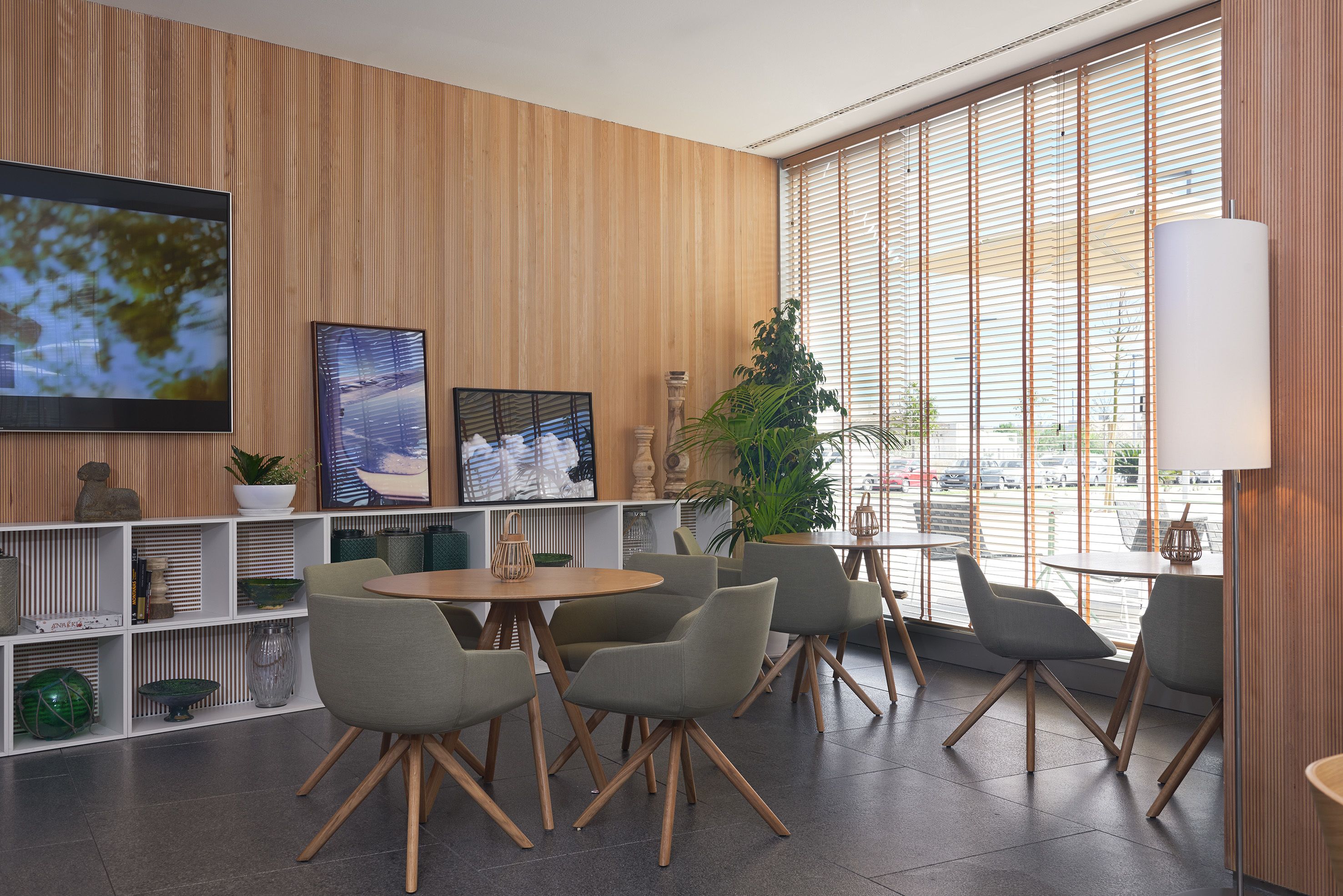 Un interior moderno con pared de madera, un televisor grande y una zona de estar con mesas y sillas.