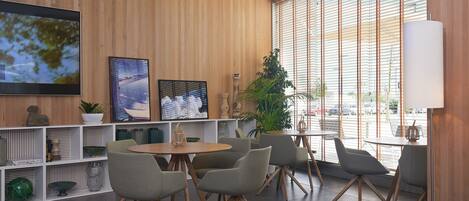Un interior moderno con pared de madera, un televisor grande y una zona de estar con mesas y sillas.