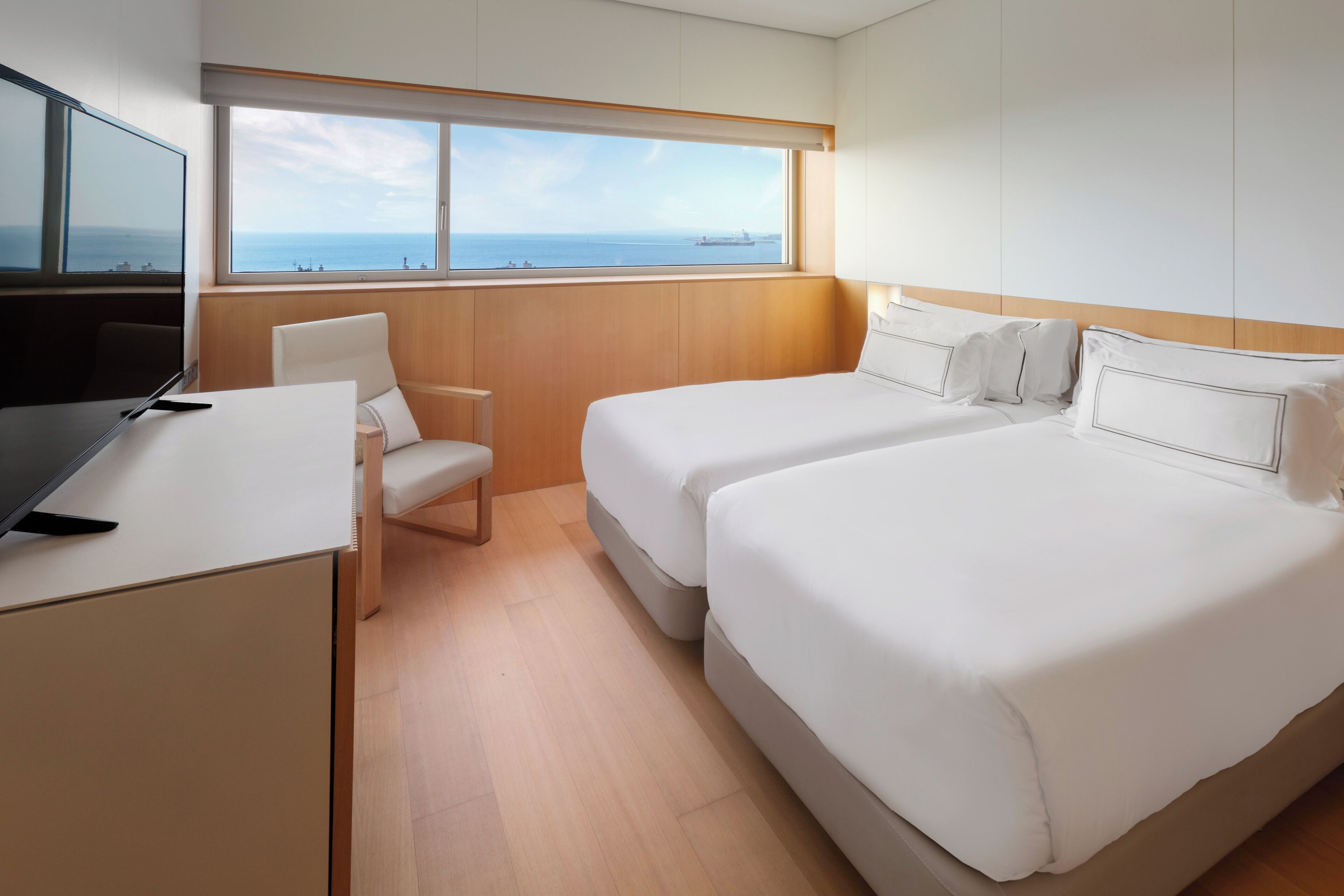 A hotel room with a large window, two beds, a desk, and a chair.