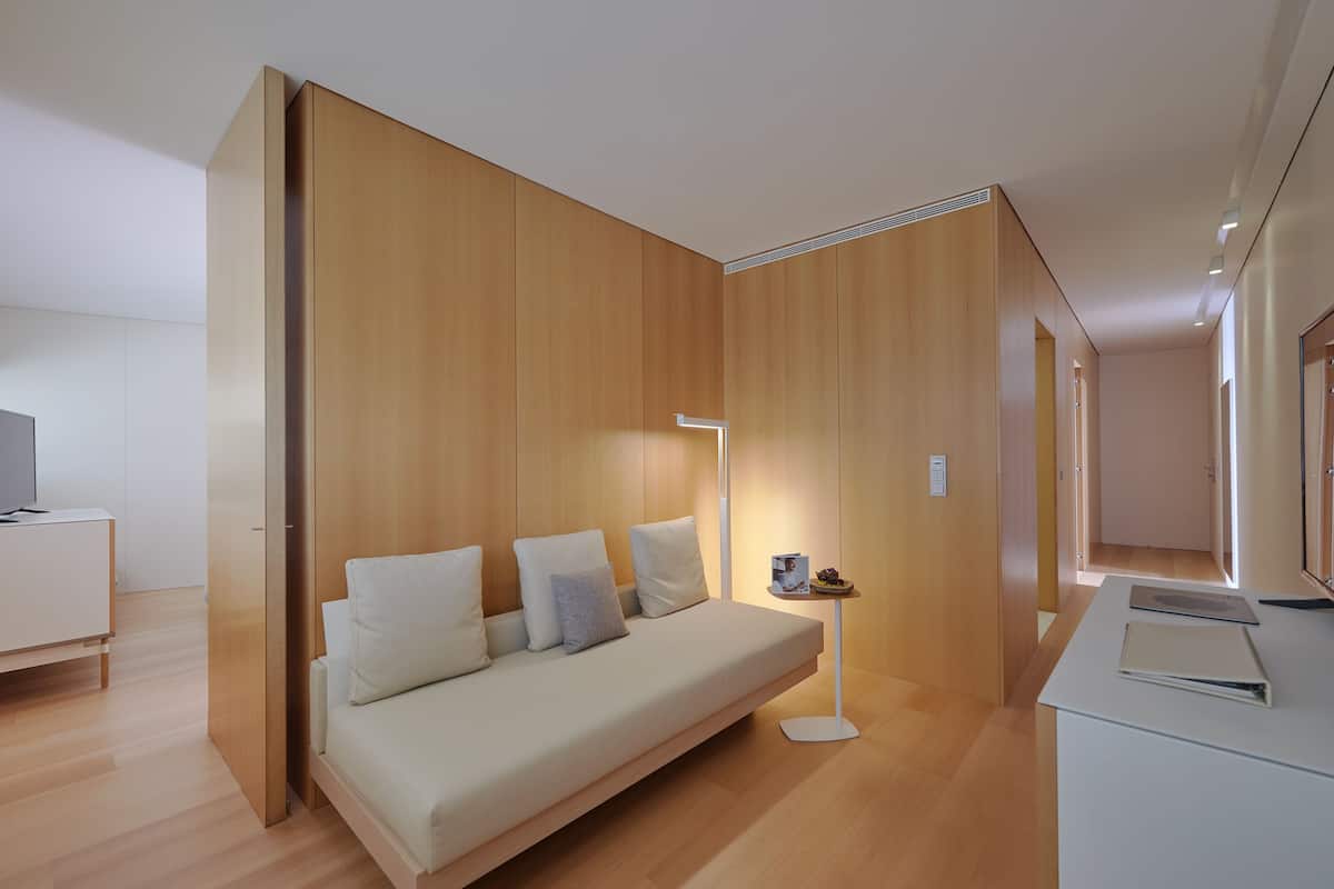 Quarto moderno com sofá, uma mesa pequena com abajur e escrivaninha.