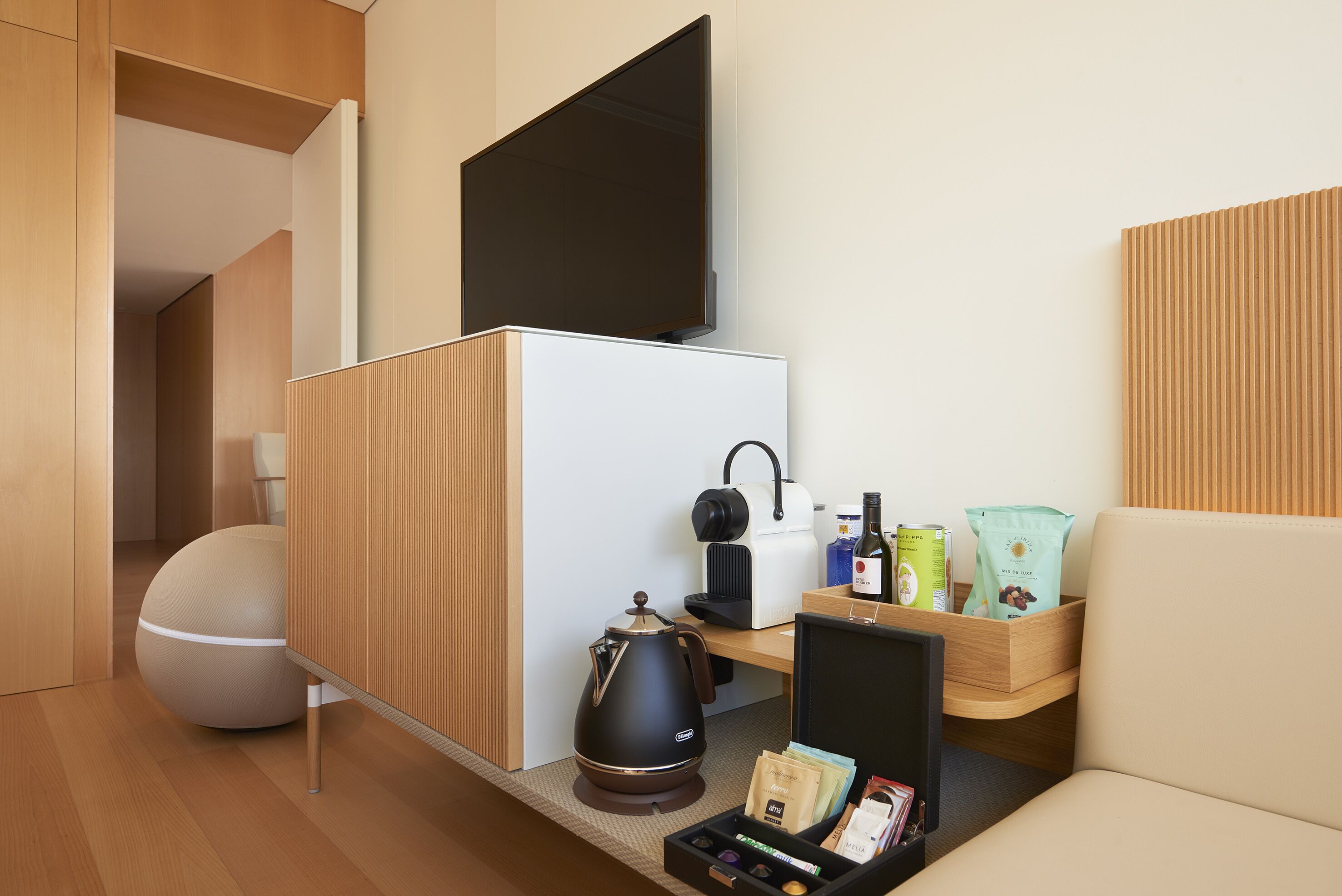 A modern, compact room with a sofa, a coffee table, a kettle, a kettle, a coffee machine, a TV, and a small cabinet with snacks and drinks.