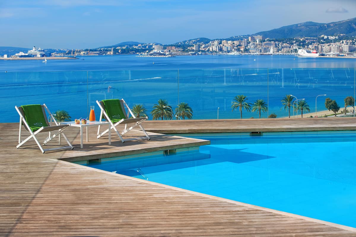 Área de piscina com espreguiçadeiras e vista para o mar e a paisagem urbana.