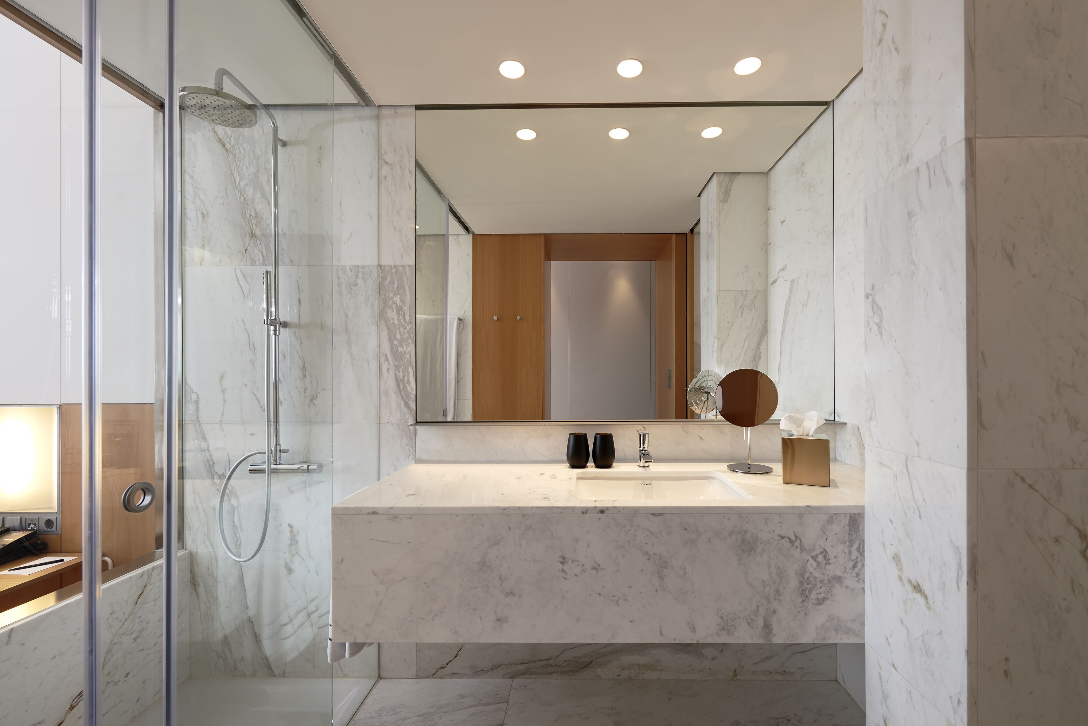 A modern bathroom with a glass-enclosed shower, a marble countertop, and a large mirror.