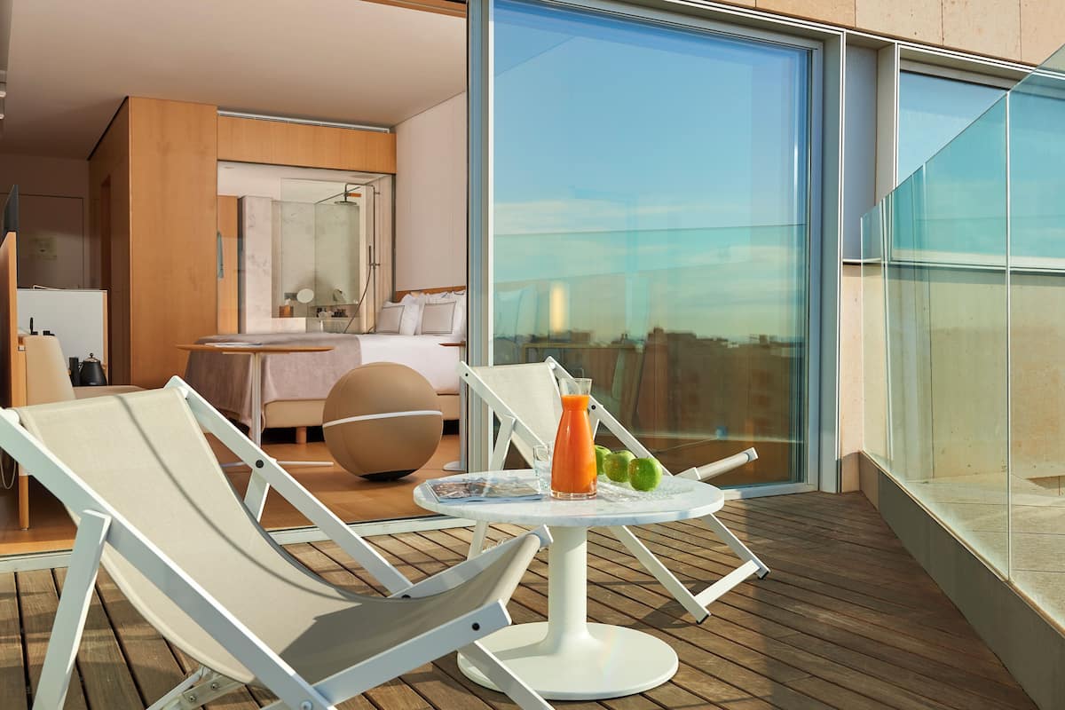 Uma varanda com cadeiras de descanso, uma mesa com bebida e vista para a cidade.