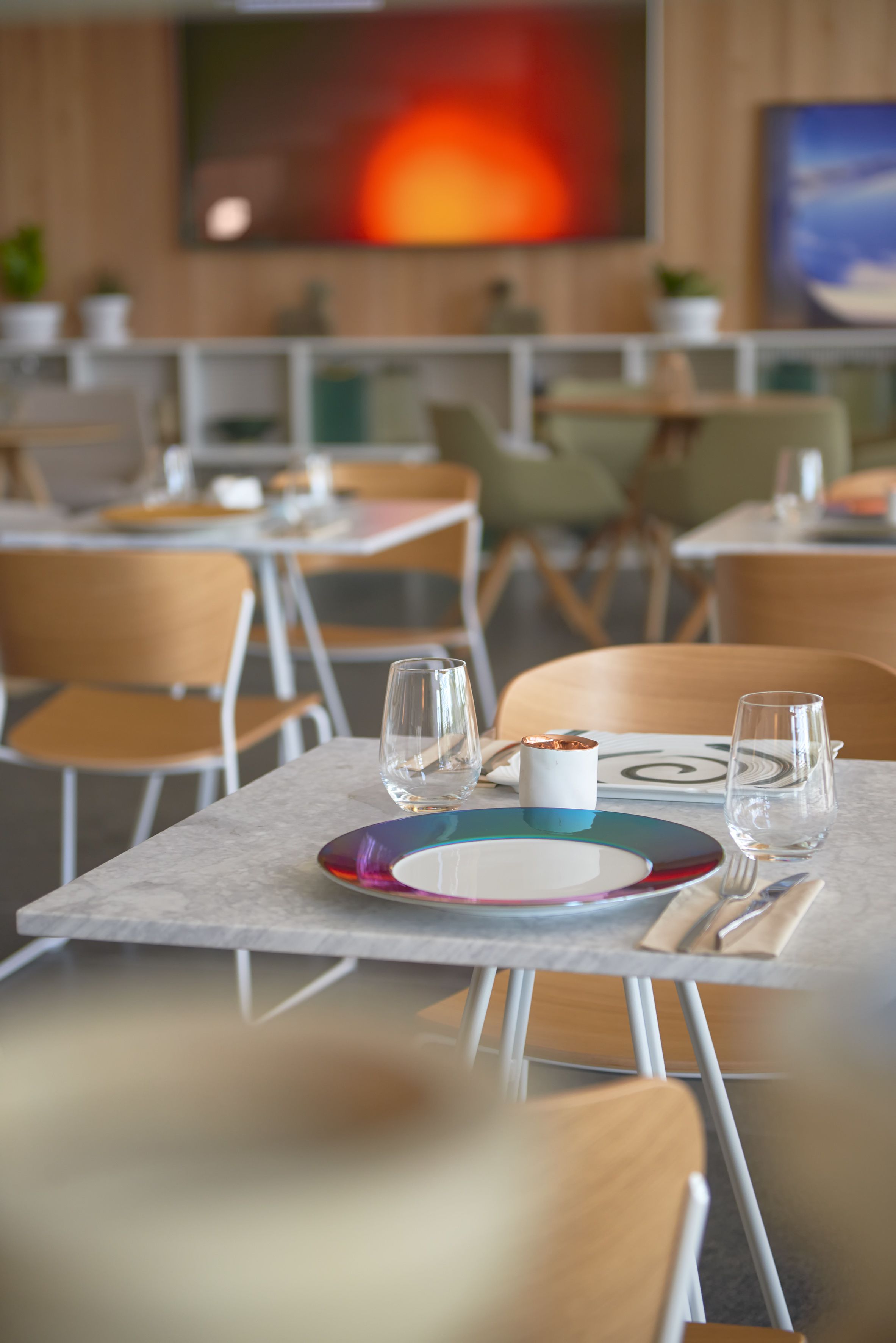 Un restaurant avec des tables dressées, des chaises et un grand tableau accroché au mur.