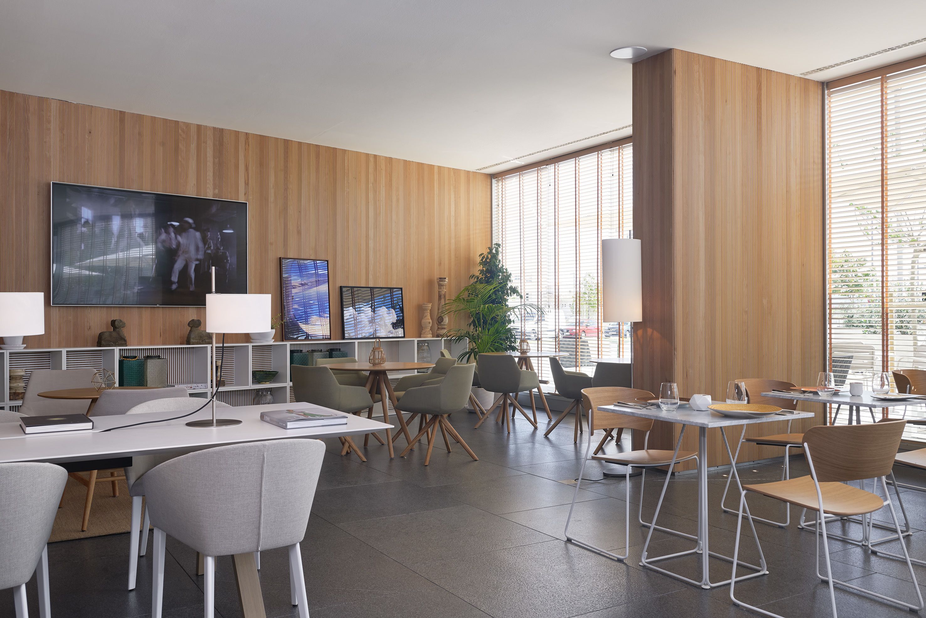 Un comedor moderno con varias mesas y sillas, un televisor de pantalla plana grande y una planta en maceta.