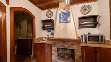 A kitchen with a stone fireplace, wooden cabinets, a microwave, and decorative tiles.