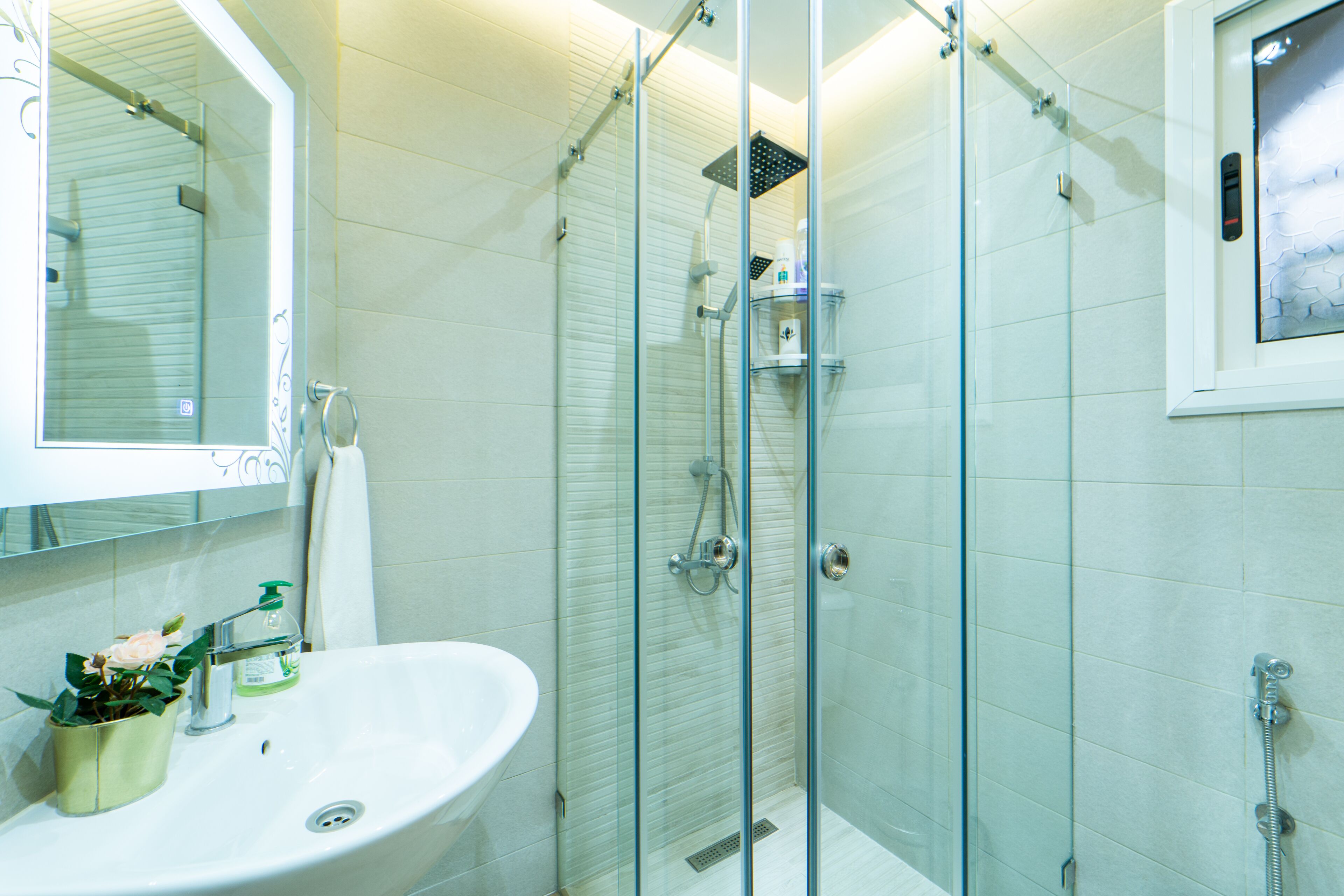 A bathroom with a glass-enclosed shower, a sink with a mirror, and a small plant.