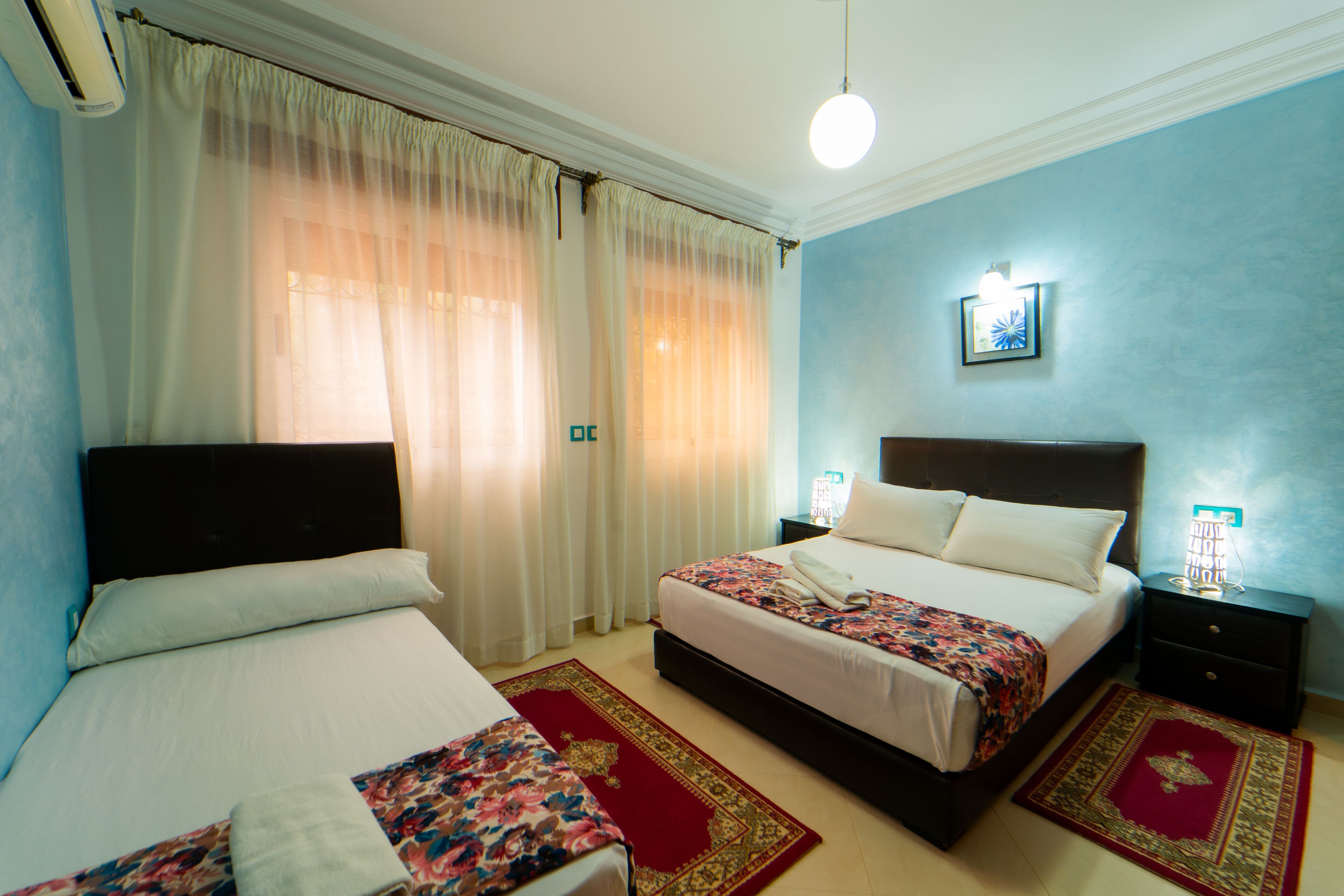 A hotel room with two beds, a red and gold carpet, and a blue wall.