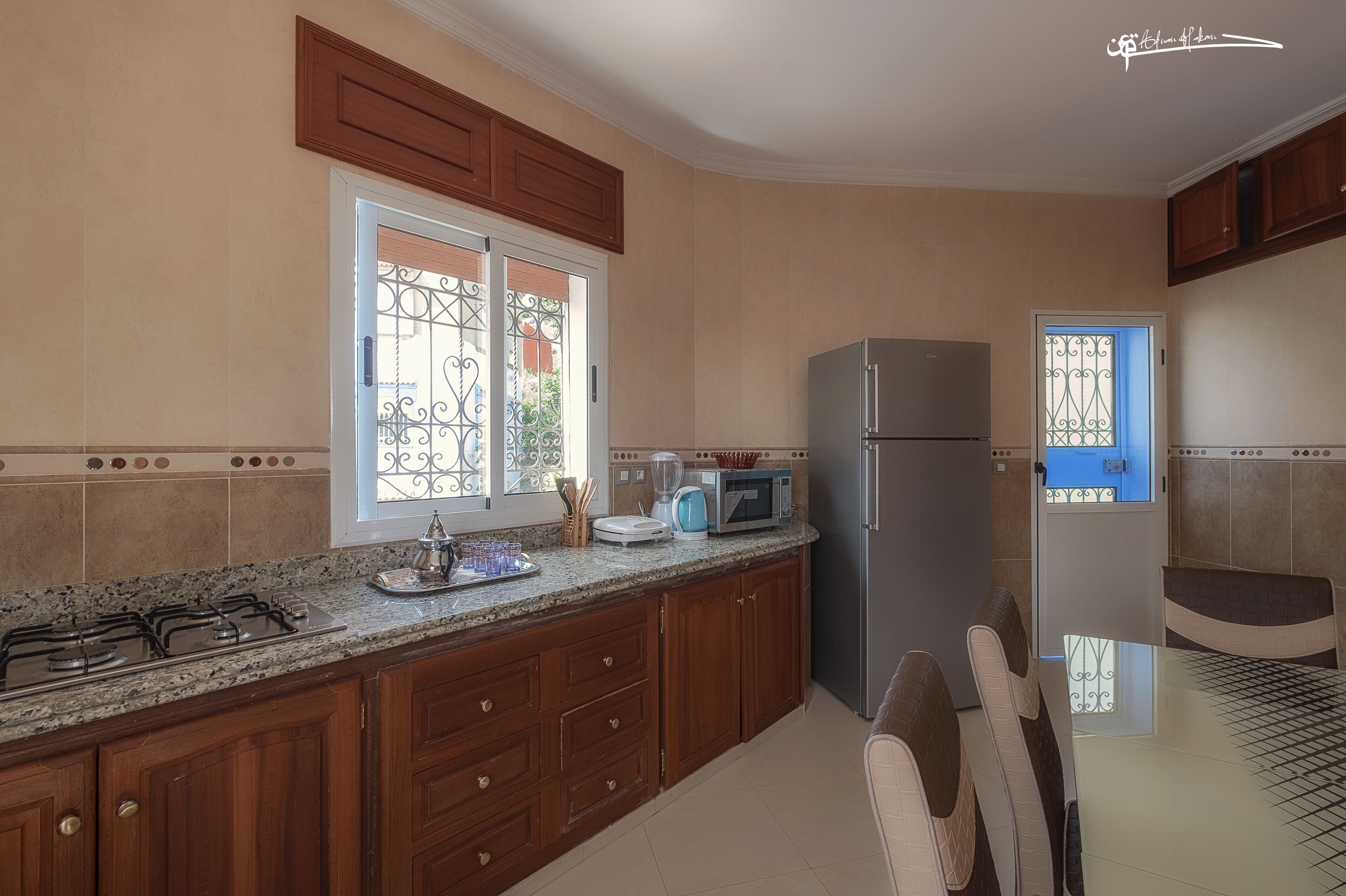 Una cocina con armarios de madera, una estufa a gas, un refrigerador y un comedor con mesa y sillas.
