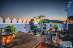 A terrace with a view of the sunset, tables, chairs, and potted plants.