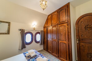 A bedroom with a bed, a wardrobe, a mirror, and two windows.