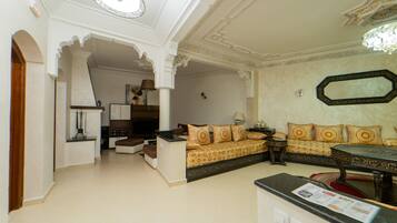 A living room with a sofa, a coffee table, and a TV. There is a door leading to another room.