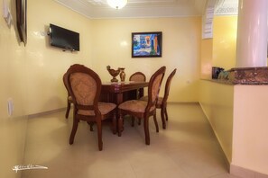 A dining area with a table and chairs, a flat-screen TV mounted on the wall, and a framed painting above the table.