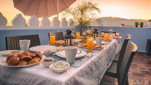 Mesa de desayuno dispuesta con platos, tazas y diferentes alimentos, con vistas a un paisaje pintoresco.
