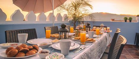 A breakfast table set with plates, cups, and a variety of food items, overlooking a scenic landscape.