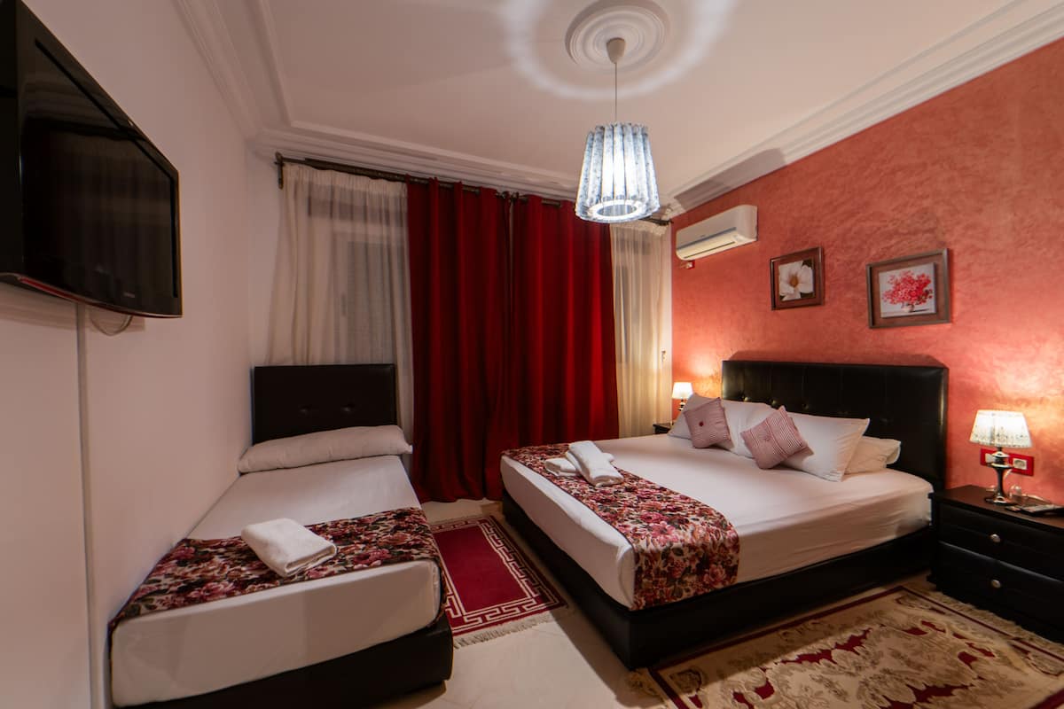 Quarto de hotel com duas camas, televisão, lustre e esquema de cores vermelho e branco.