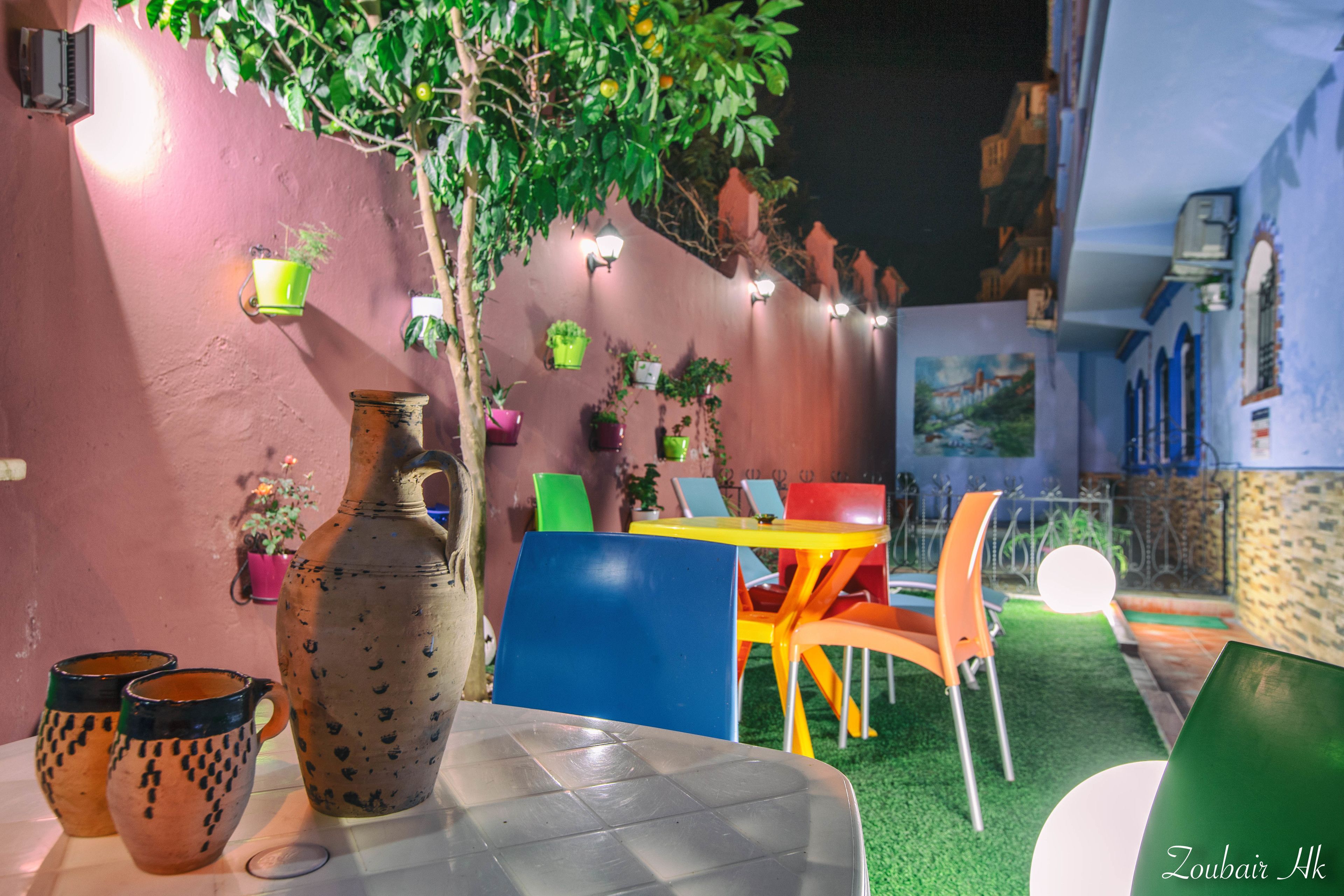 An outdoor dining area with a table and chairs, surrounded by potted plants and a decorative wall.