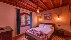 Un dormitorio con techo de madera, una cama con ropa de cama blanca, una mesita de noche, un aparador y una ventana con cortinas azules.