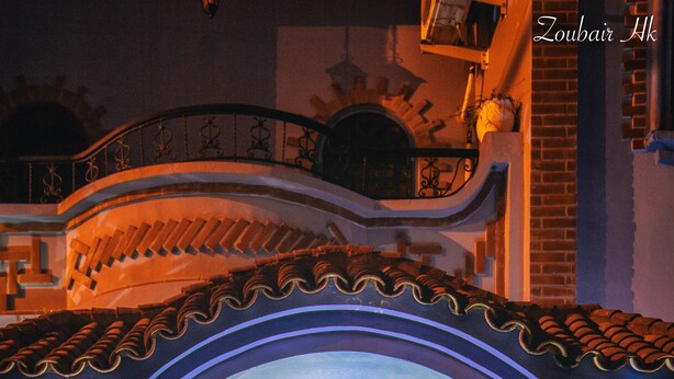 Una entrada azul en arco con columnas decoradas, suelo de baldosas y una lámpara colgante.