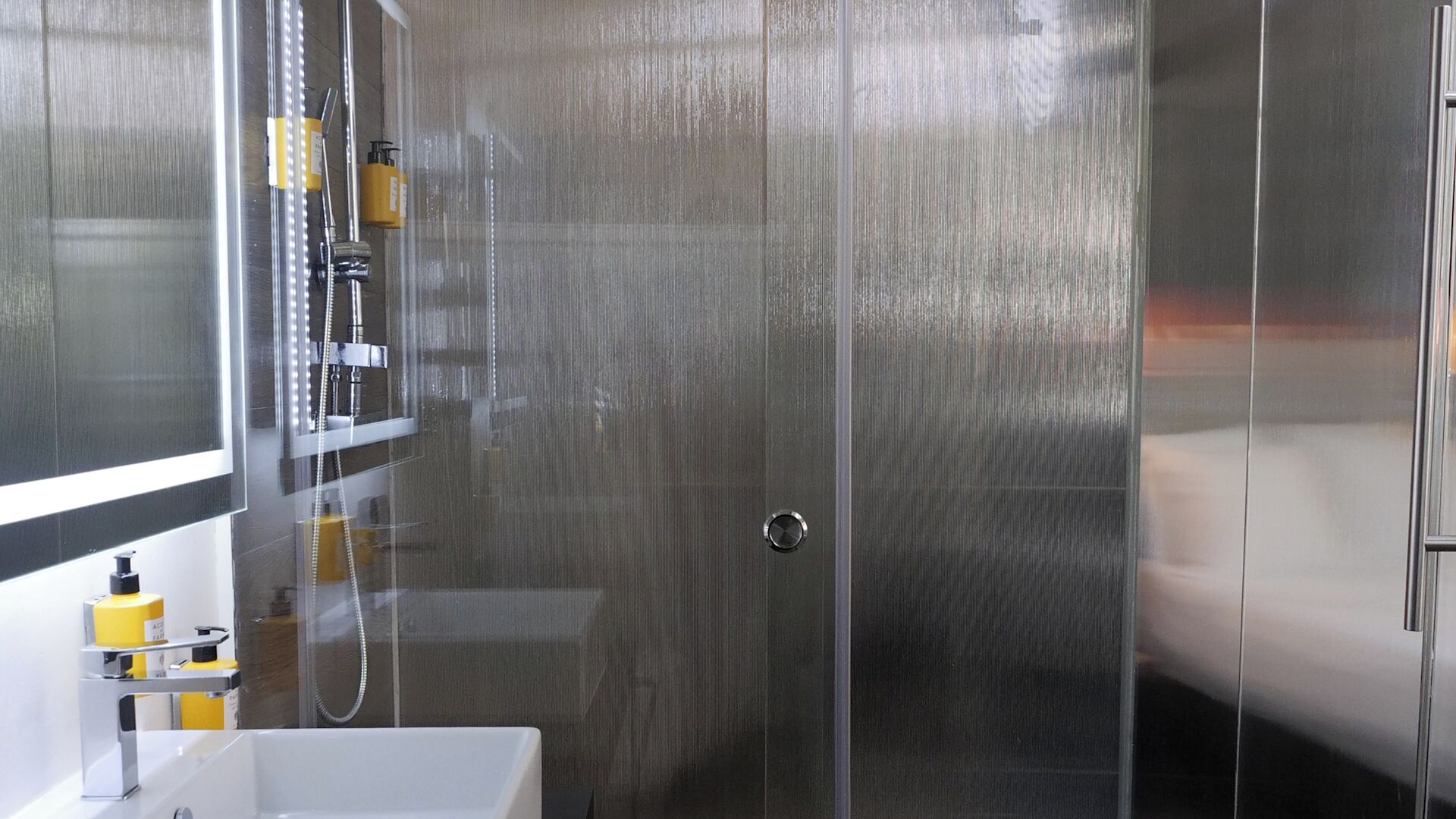 A modern bathroom with a glass shower enclosure, a white sink, and toiletries on the side.