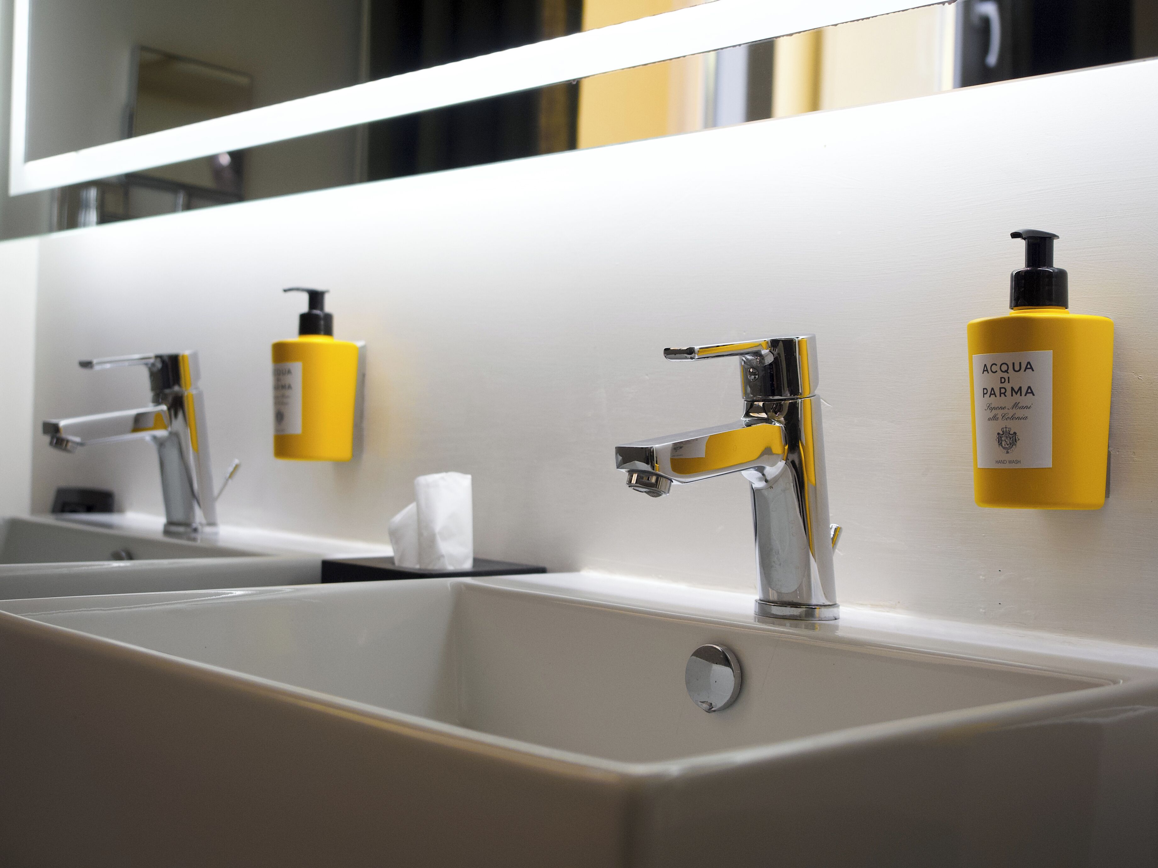 A modern bathroom with three sinks, each with a chrome faucet and a yellow soap dispenser.