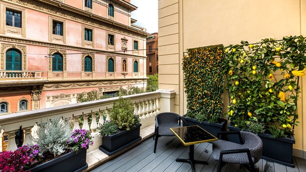 A balcony with outdoor seating, a decorative wall with plants, and a historic building in the background. - Hotel The Haven Roma (Rome)