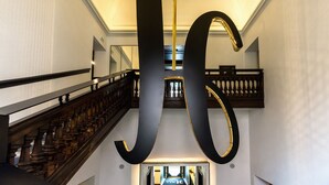 A grand staircase with a modern chandelier and a large, bold letter 'L' suspended above. - Hotel The Haven Roma (Rome)