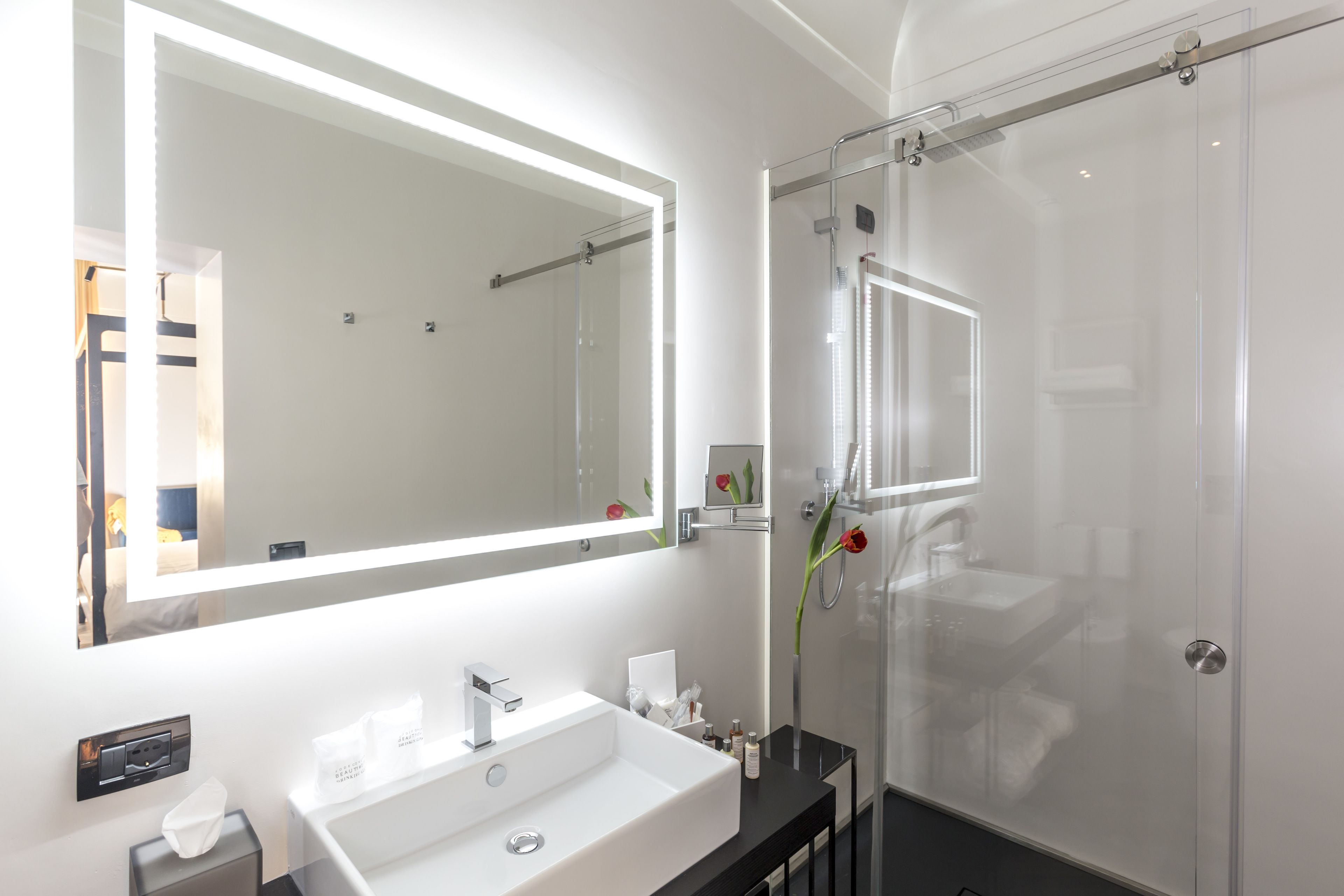 Een moderne badkamer met een grote spiegel, een witte wastafel en een douche met glazen wanden.