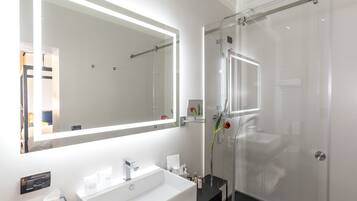 Een moderne badkamer met een grote spiegel, een witte wastafel en een douche met glazen wanden.