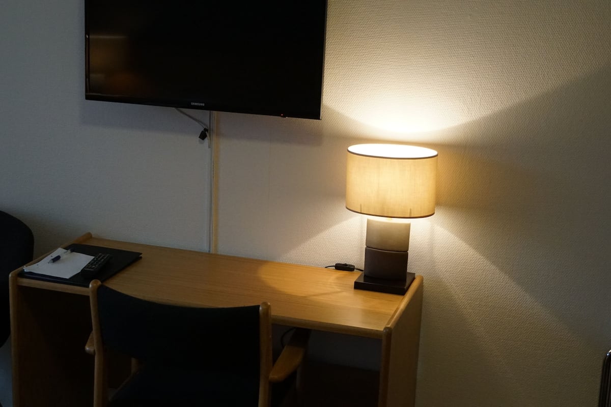 A small desk with a lamp, a chair, and a flat-screen TV mounted on the wall.