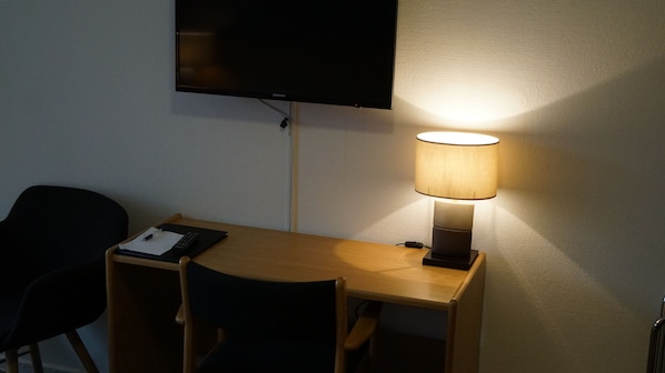 A small desk with a lamp, a chair, and a flat-screen TV mounted on the wall.