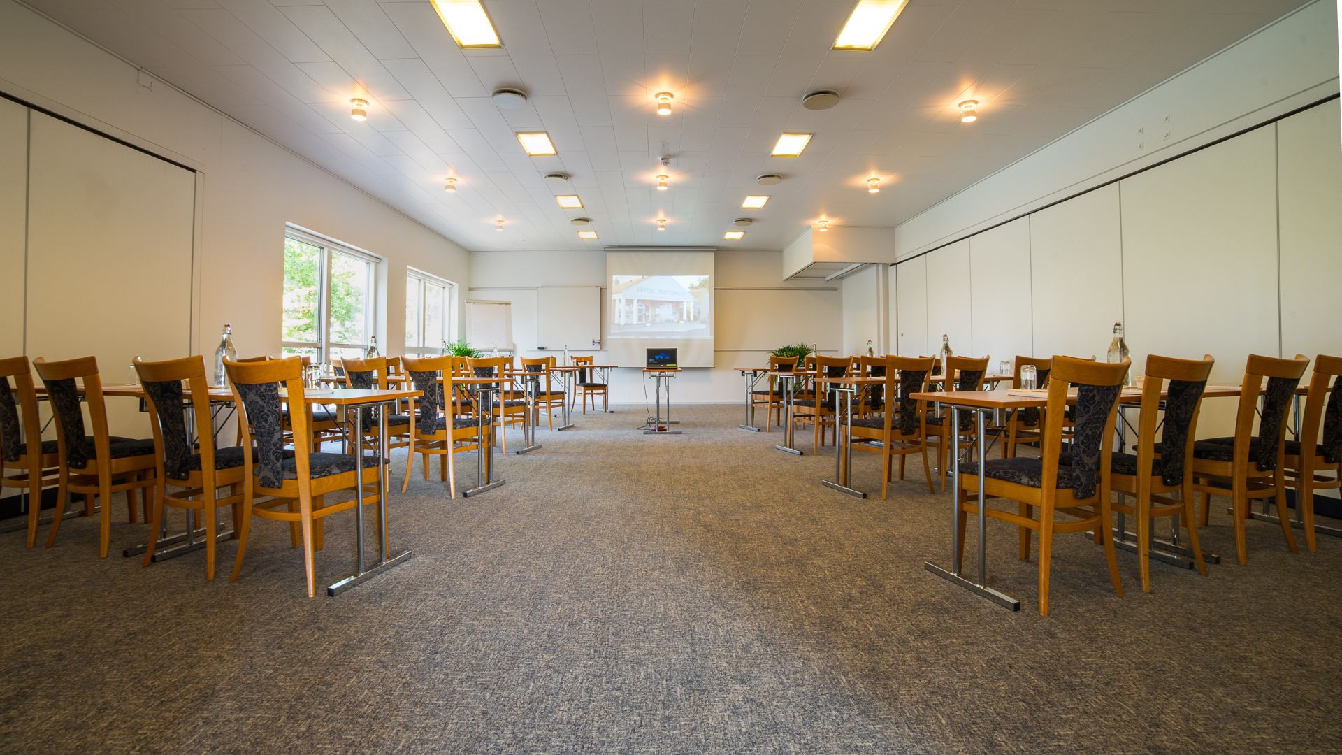 A conference room with multiple tables and chairs, a projector screen, and a carpeted floor.