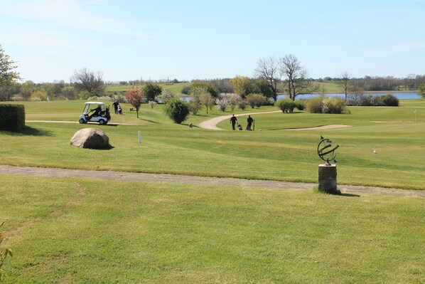 A golf course with a clear path, a golf cart, and a sculpture. - Hotel Præstekilde (Stege)