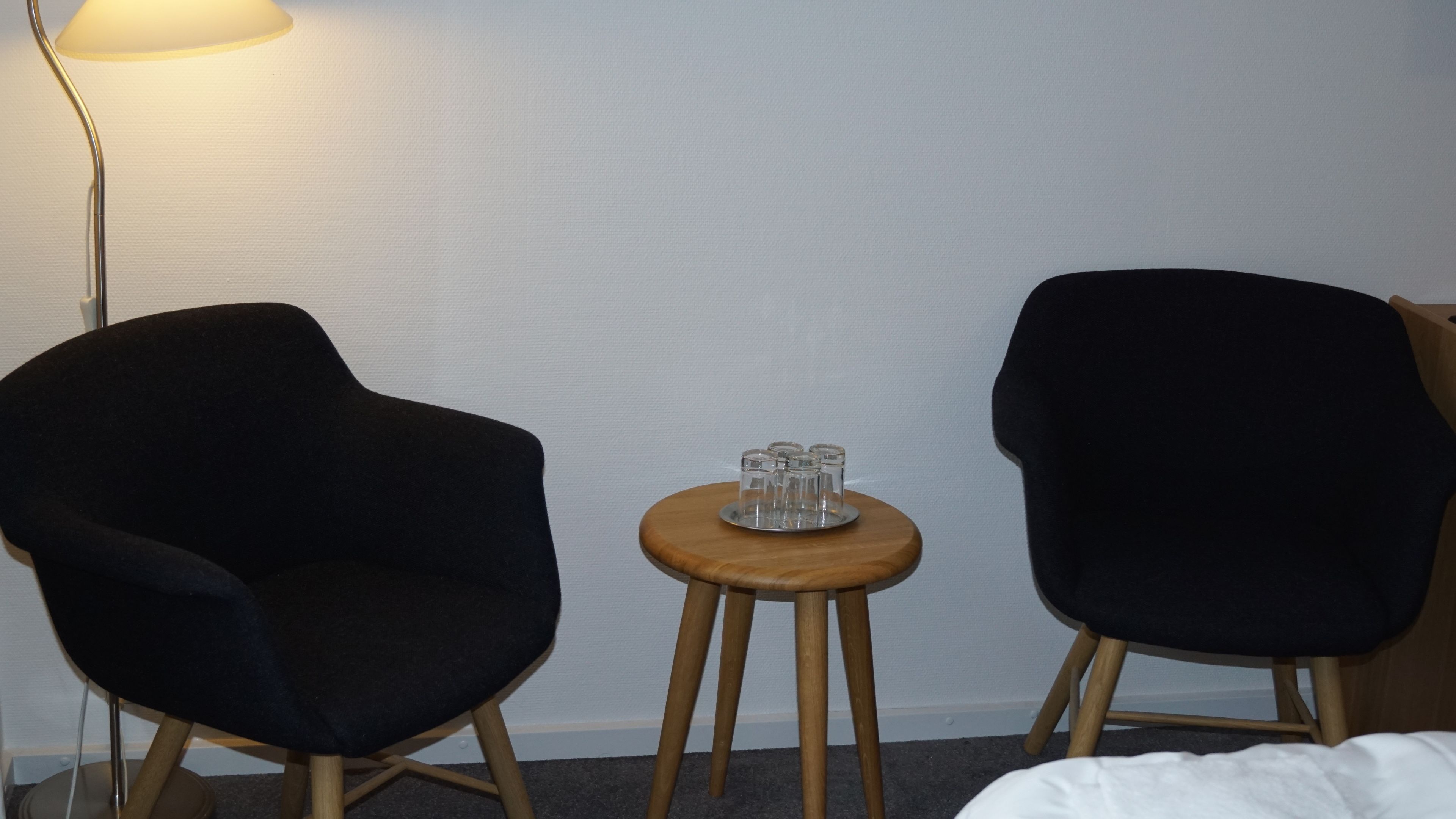 A room with two black armchairs, a small wooden table with a glass set, and a floor lamp.