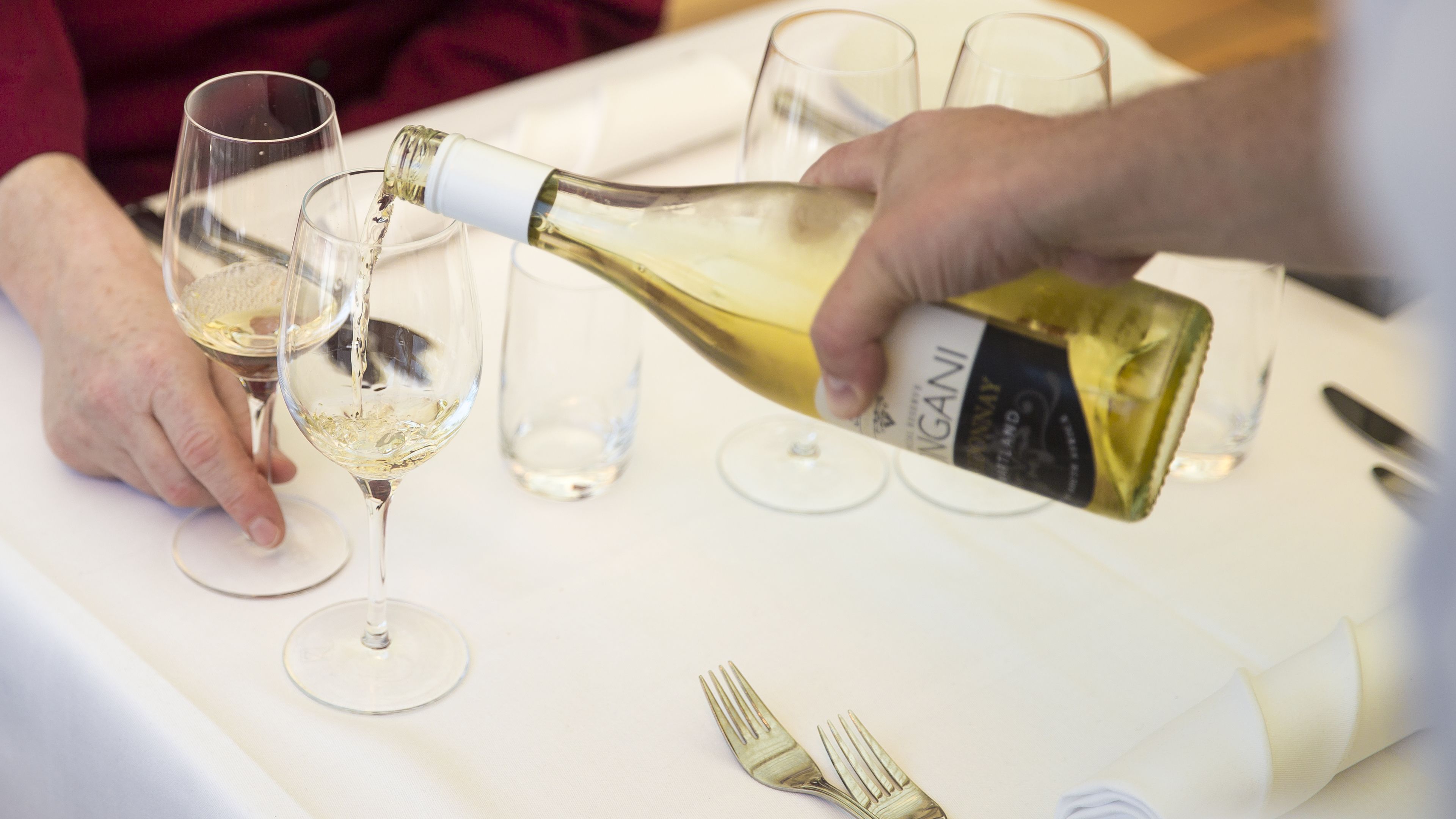 Una persona sirviendo vino blanco en una copa.