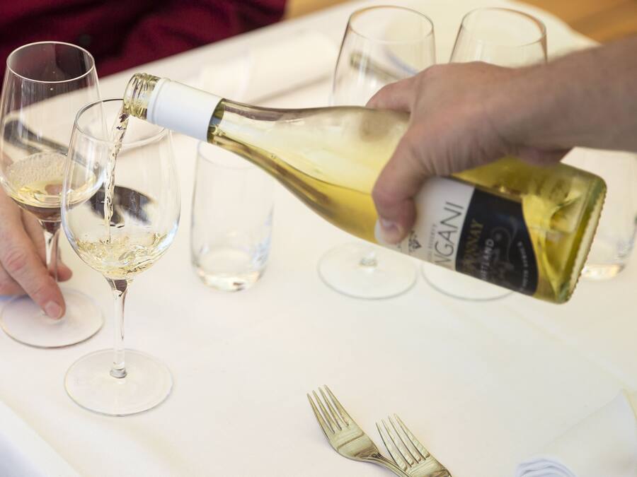 Una persona sirviendo vino blanco en una copa.