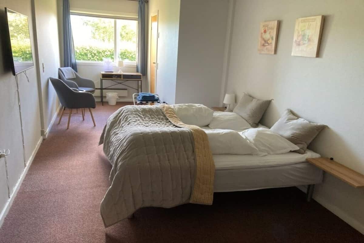 A bedroom with a bed, a desk with a chair, a window, and a door.