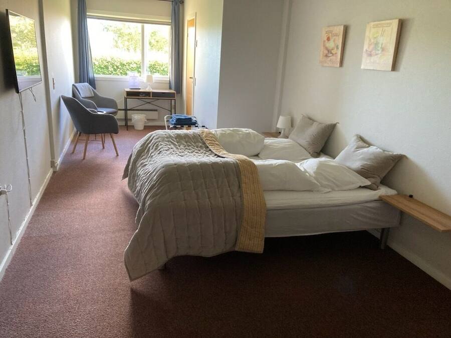 Een slaapkamer met een bed, een bureau met stoel, een raam en een deur.