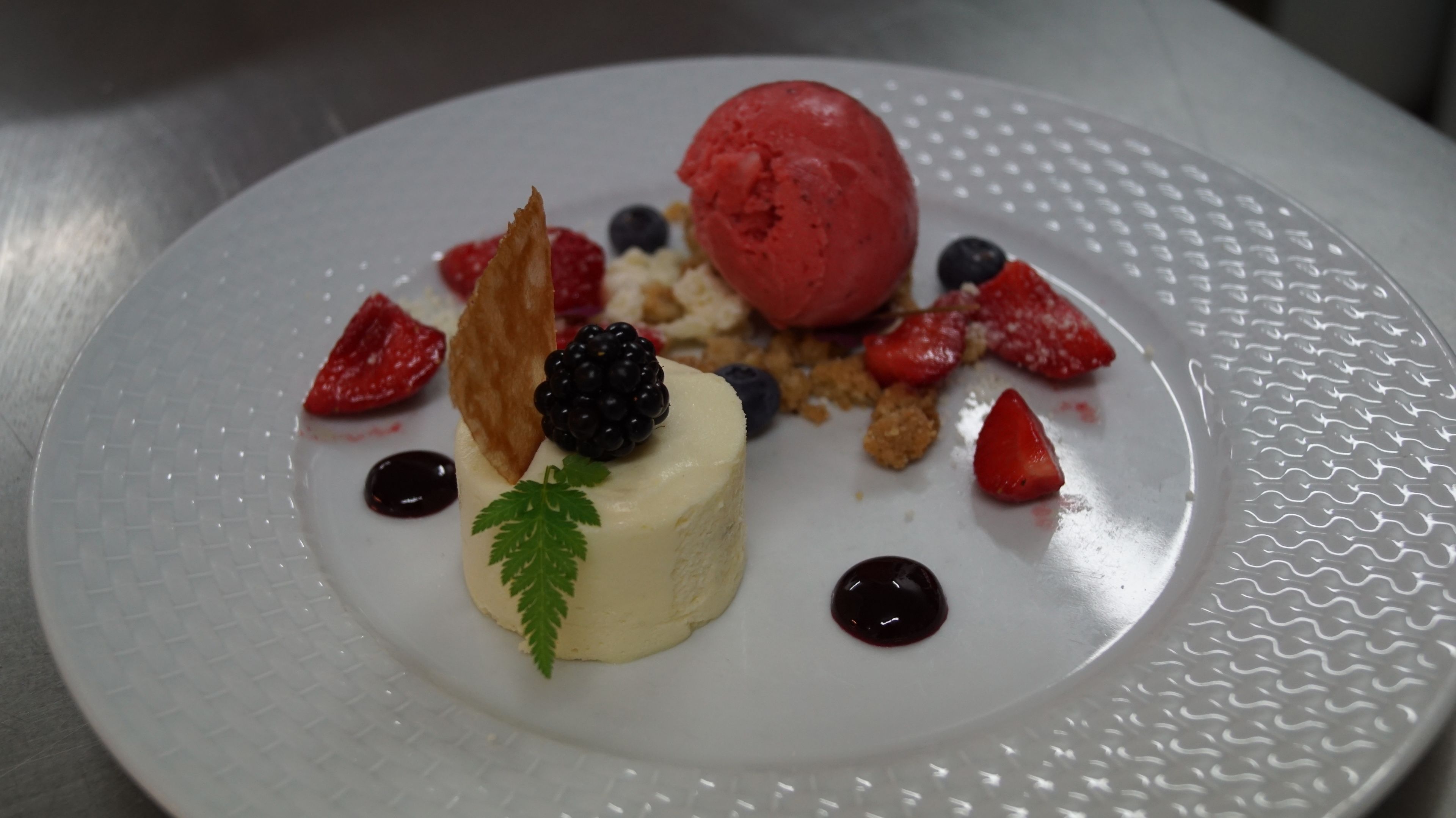 Un plato de postre con una porción de helado, fresas, zarzamoras y una pequeña decoración de hoja.